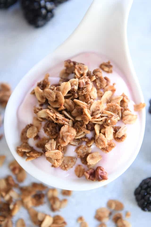 White deep spoon with strawberry yogurt and cinnamon granola.