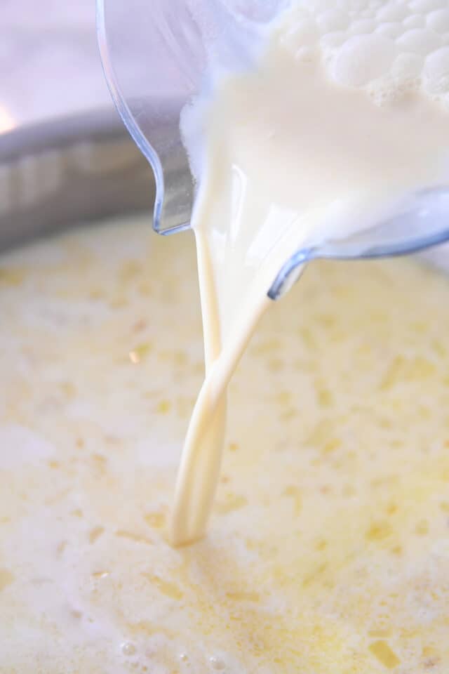 Pouring milk and flour mixture into saucepan with onions and garlic.