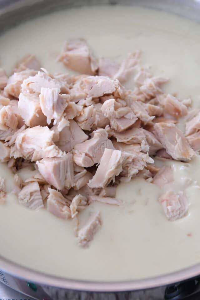 Cubed, cooked chicken in saucepan with white gravy.