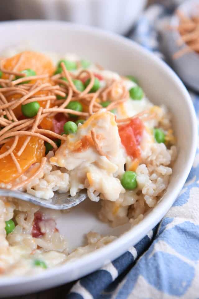 White shallow bowl with fork taking bite of rice, chicken gravy, peas, and cheese.