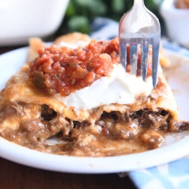 Two saucy enchiladas on white plate with fork.