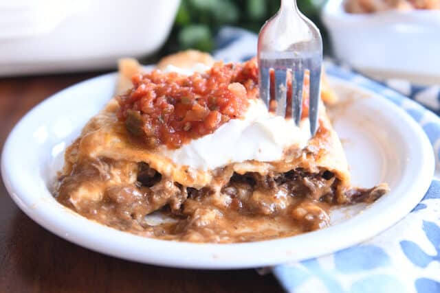 Two saucy enchiladas on white plate with fork.