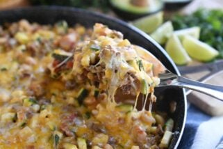 serving spoon lifting up cheesy portion of zucchini skillet