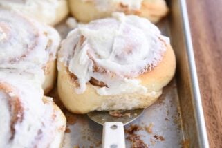 spatula lifting up baked frosted cinnamon roll on sheet pan