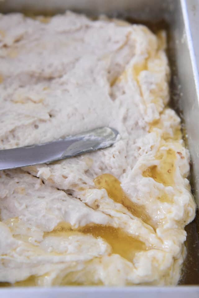 Spreading biscuit batter in pan with melted butter.