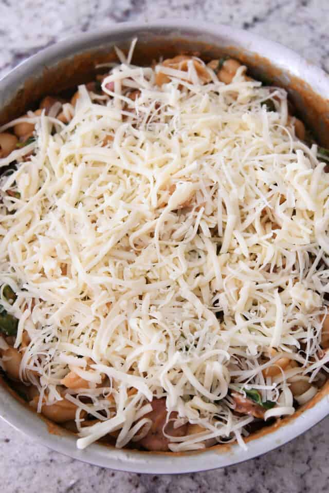 Shredded mozzarella cheese on top of pasta ingredients in pan.