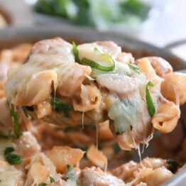 Spoon scooping up portion of pasta shells, sausage, cheese and basil.