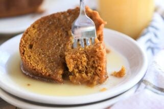 Bite of orange pumpkin cake being scooped out of big slice with fork on white plate.