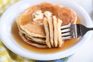 Four sourdough pancakes on white plate with fork piercing several pieces.