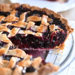 Triple berry pie in glass pie dish with one piece removed.