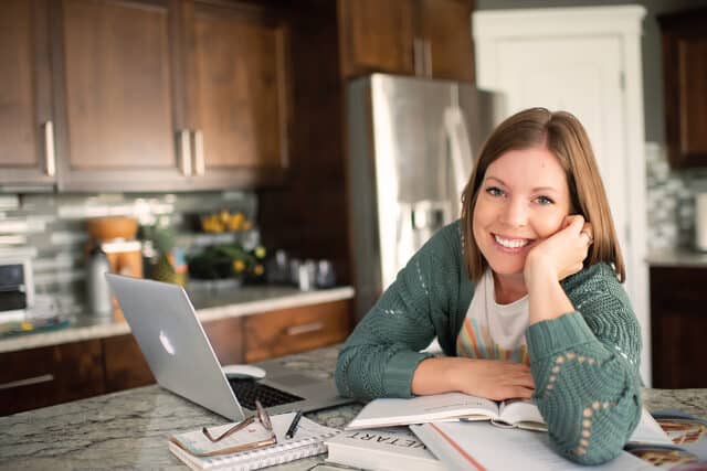 woman reading cookbooks at counter with laptop