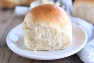 Baked soft and fluffy dinner roll on white plate.