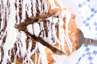 Slice of apple pie with pecans on top and drizzled with glaze.