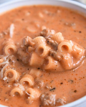 Spoon scooping up bite of soup with tomatoes, noodles, and ground beef.