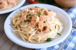 Cooked shrimp on creamy linguine on white plate.
