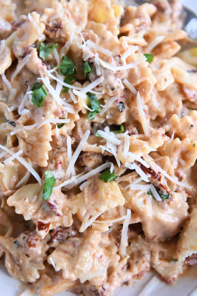 Jumble of bowtie pasta noodles with pasta sauce, parmesan cheese and basil.