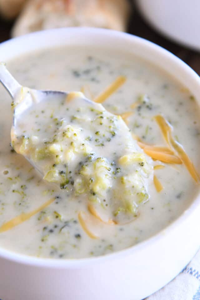 Spoon scooping bite of broccoli cheese soup in white bowl.
