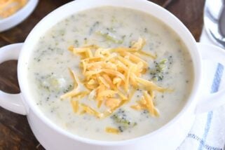 Broccoli cheese soup in white bowl with cheddar cheese.