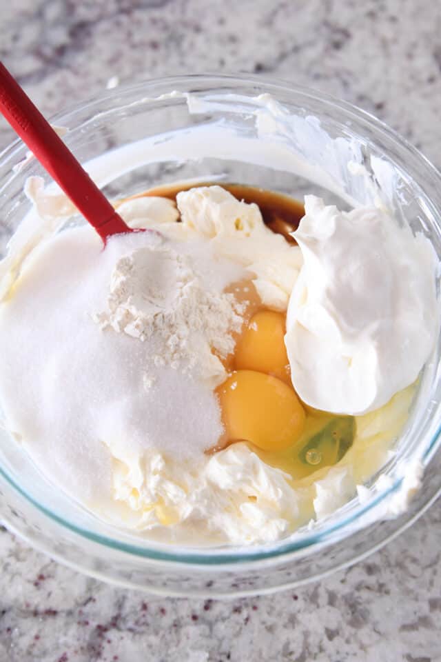 Eggs, sugar, cream cheese, sour cream, and flour in glass bowl.