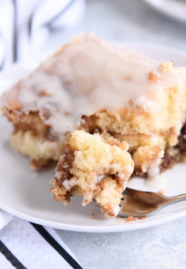 Bite of cinnamon roll cake on fork on white plate.