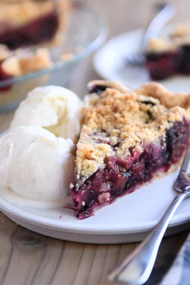 Triple berry pie on white plate with scoop of vanilla ice cream.
