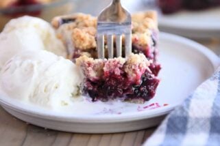 Fork taking bite of berry rhubarb pie and vanilla ice cream on gray plate.