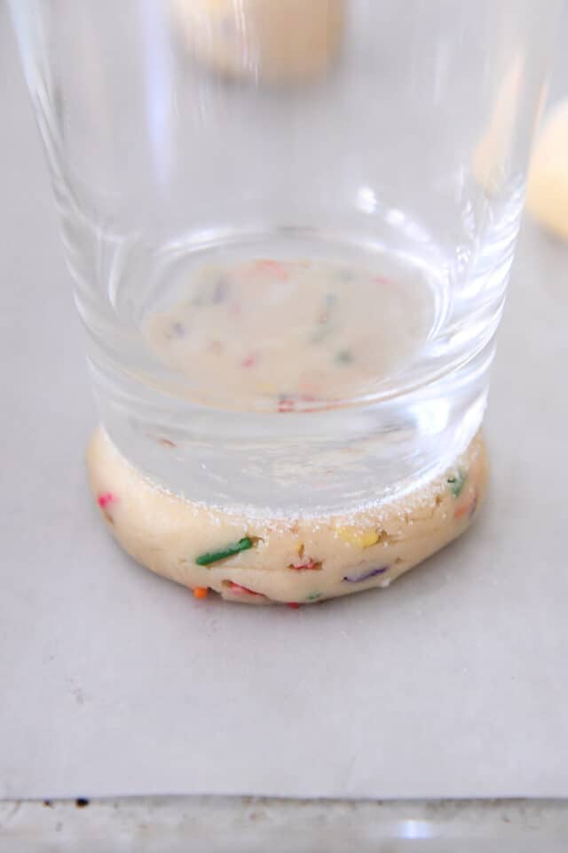 Pressing sugar cookie dough into thick circle with glass dipped in sugar.