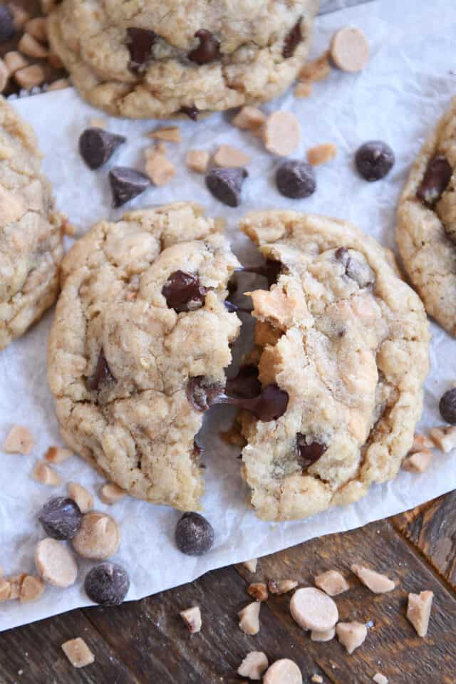 Cookie broken in half with melty chocolate chips on white parchment paper.