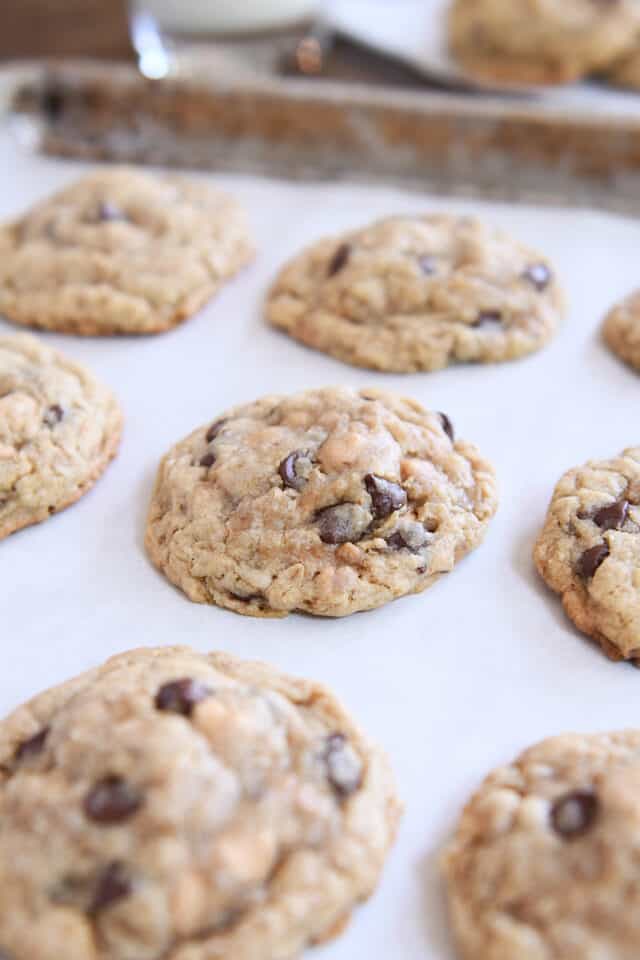 Five or six large oatmeal chocolate chip cookies with peanut butter and toffee on parchment lined baking tray.