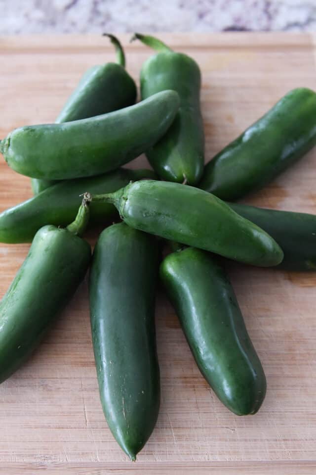 Ten jalapenos on wood cutting board.