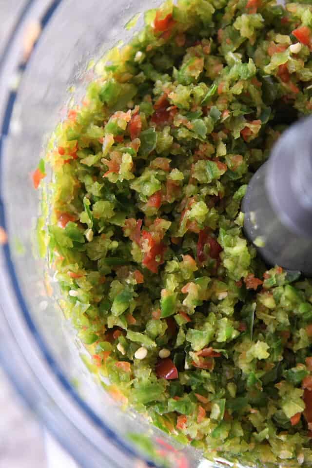 Food processor with blade filled with chopped bell peppers and jalapenos.