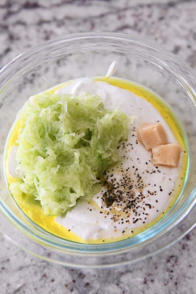 Glass bowl with yogurt, garlic, pepper and shredded cucumber.