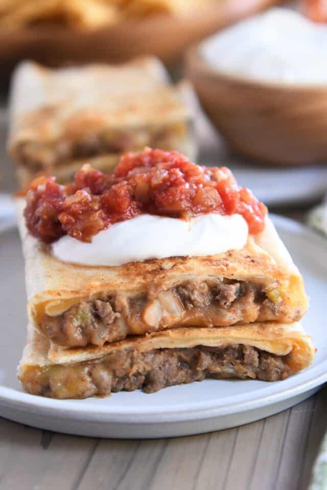 Beef and bean wrap in half on gray plate with salsa and sour cream.