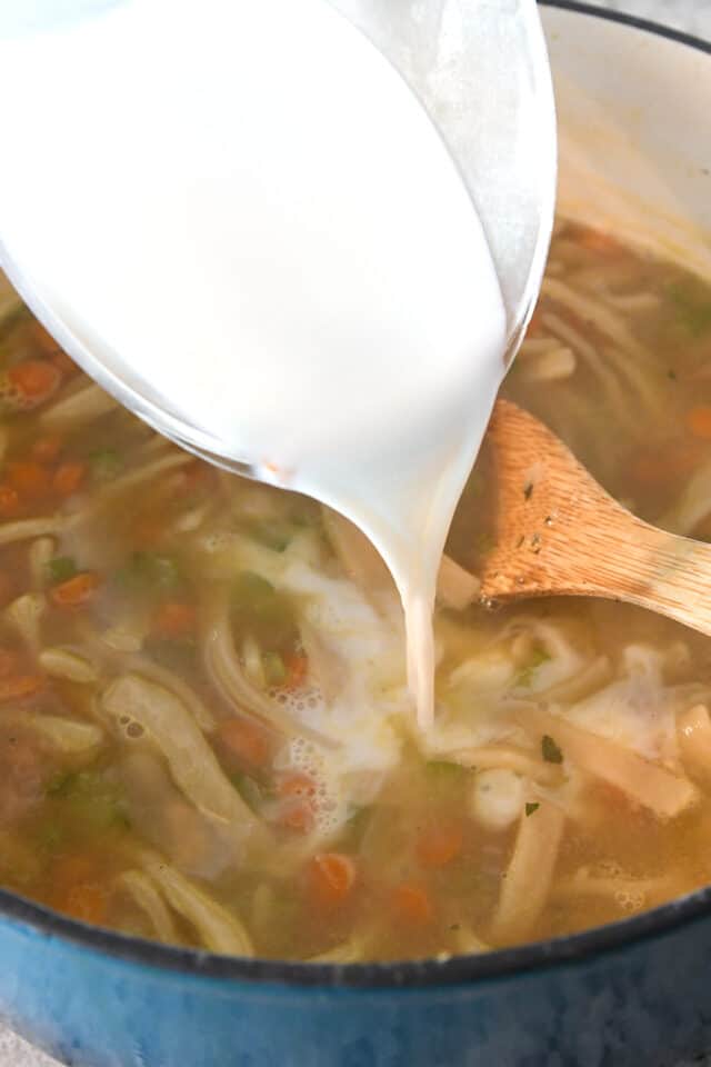 Pouring milk into chicken noodle soup.