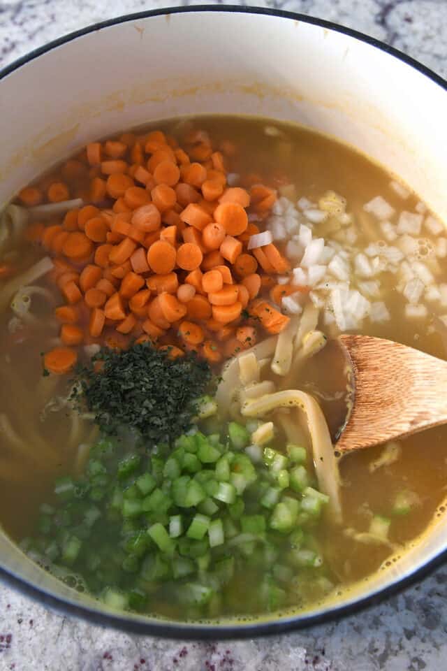 Soup pot with carrots, celery, onion, parsley, broth and noodles.