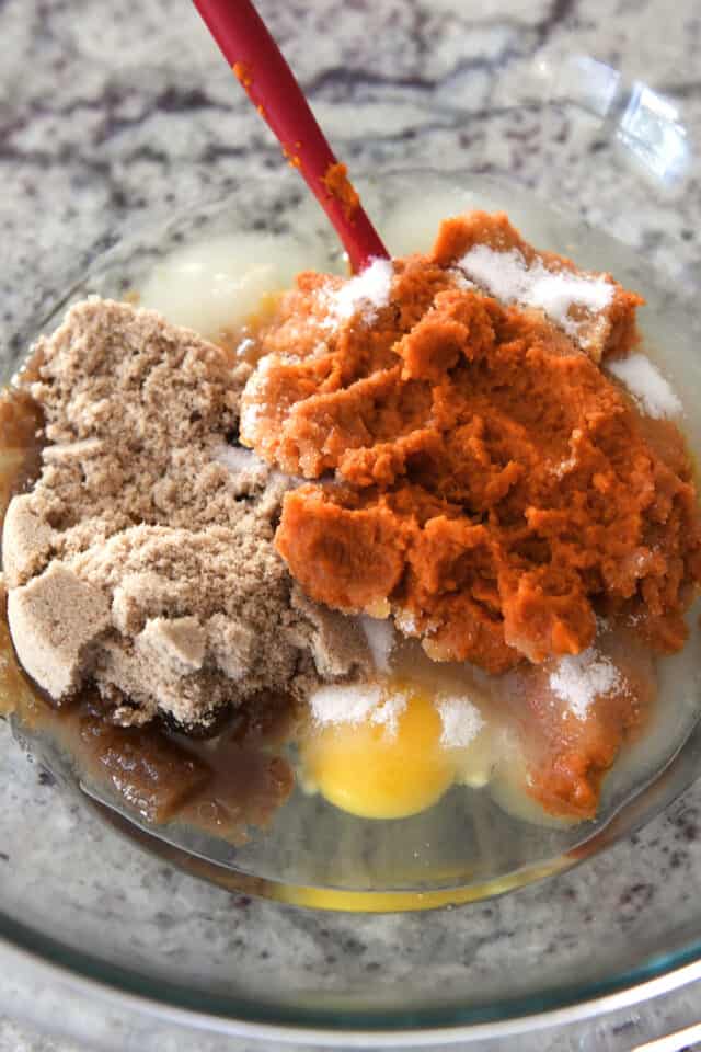 Brown sugar, eggs, pumpkin puree and sugar in glass bowl.