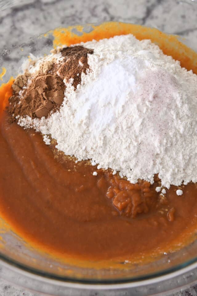 Mixing batter for pumpkin muffins in glass bowl with pumpkin puree, eggs, oil, flour and spices.