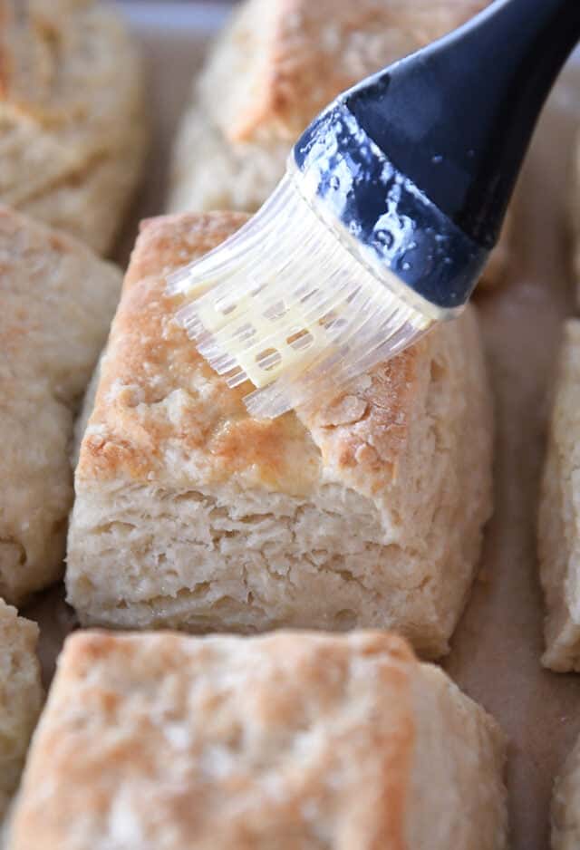 Brushing melted butter on top of baked biscuits.