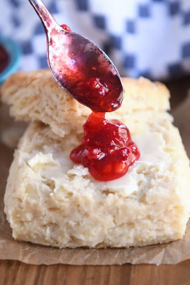 Dolloping raspberry jam onto buttered biscuit.