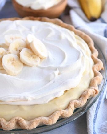 Whole banana cream pie topped with sliced bananas and whipped cream.