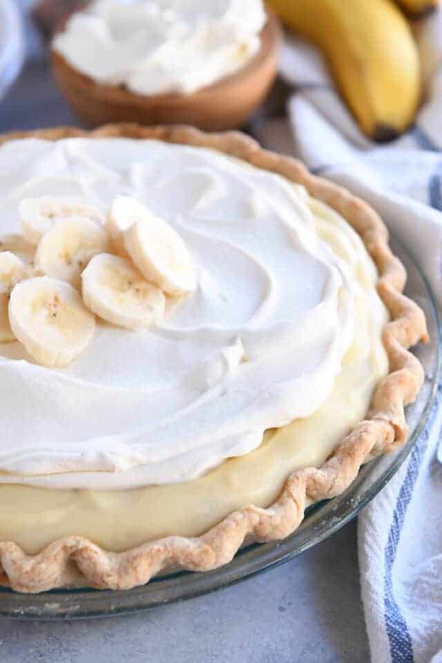 Whole banana cream pie topped with sliced bananas and whipped cream.