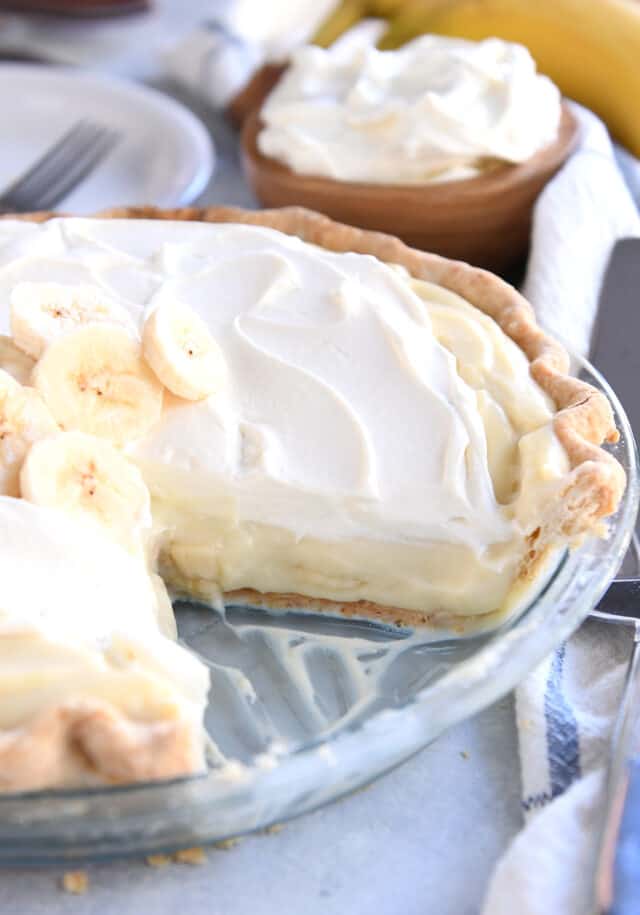 Piece removed from banana cream pie in glass pie plate.