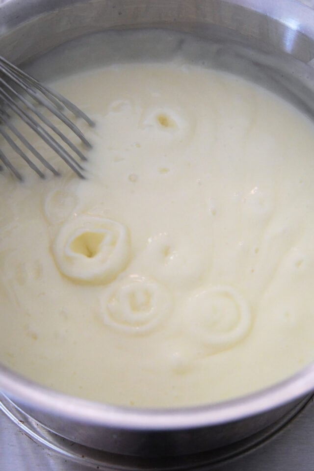 Custard bubbling with whisk in stainless pot.
