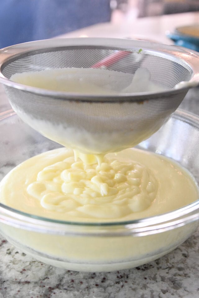 Straining vanilla custard pudding in fine mesh strainer into glass bowl.