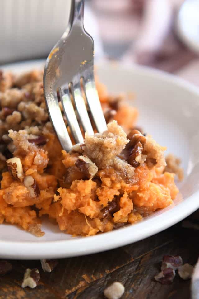 Fork scooping bite of sweet potato casserole with pecan topping.