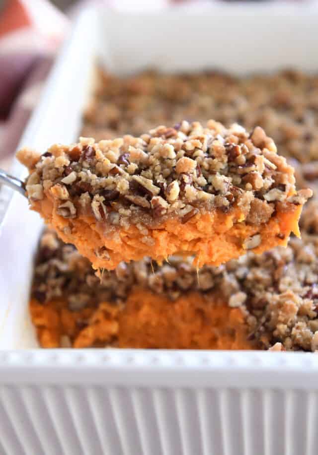 Serving spoon with scoop of sweet potato casserole and pecan topping.