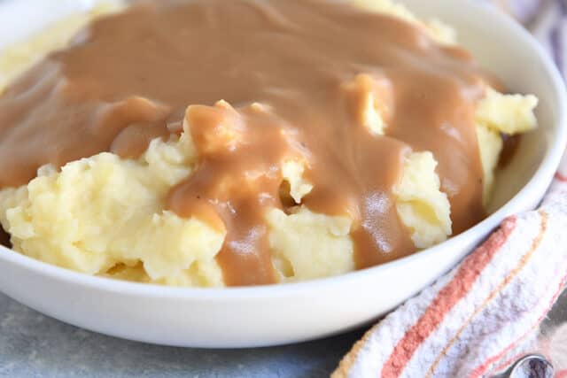 White bowl with mashed potatoes and brown gravy.