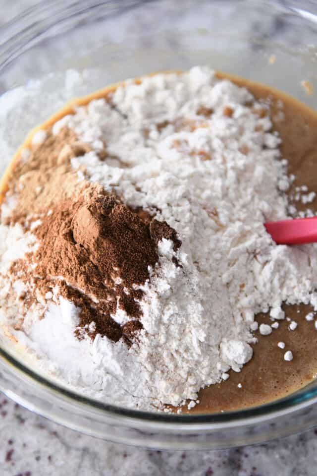 Glass bowl with gingerbread batter, flour, cinnamon nutmeg and allspice.