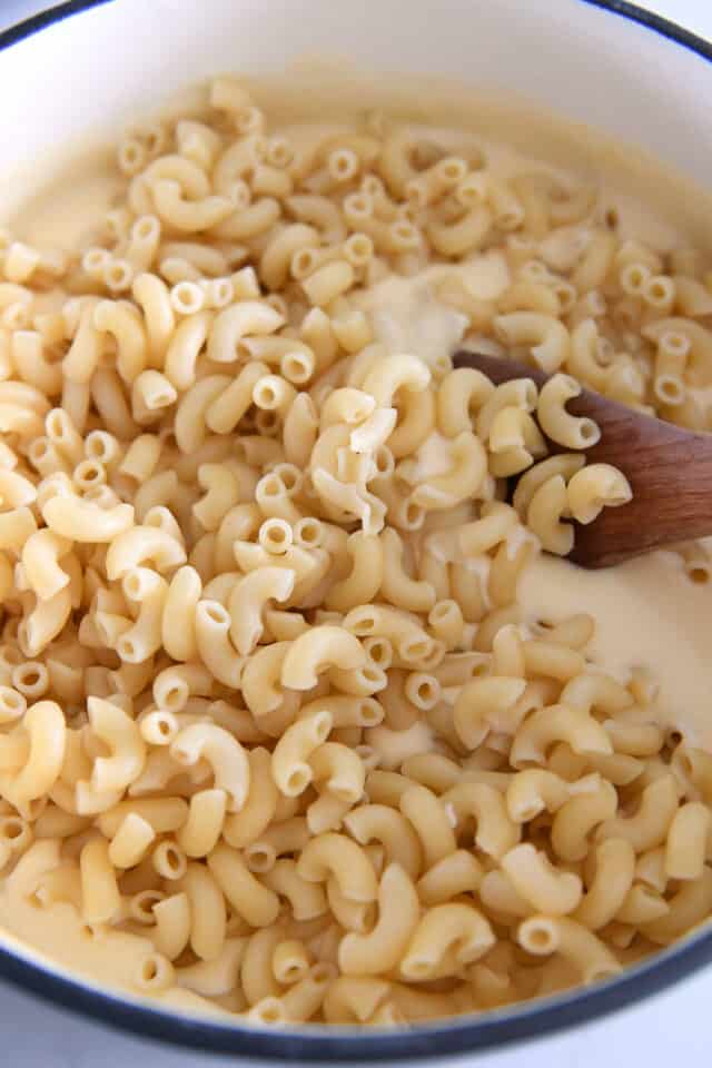 Macaroni noodles added to cheese sauce in large pot.