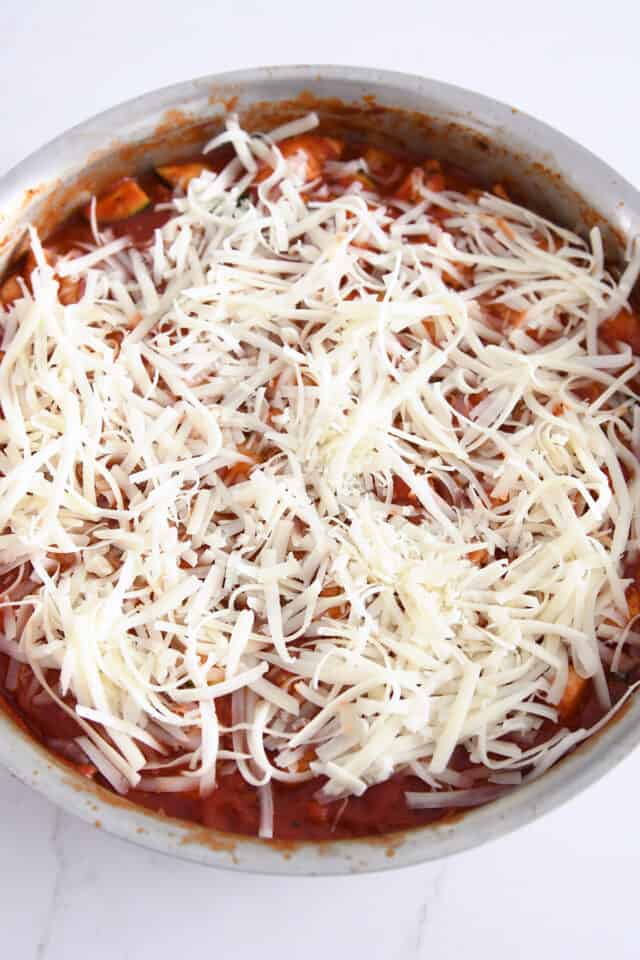 Mozzarella cheese on top of tomato sauce in stainless skillet.